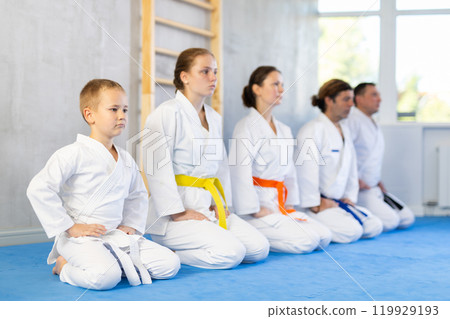 Group of people in kimono with master in sitting position during group karate training Group of people in kimono with master in sitting position during group karate training 119929193