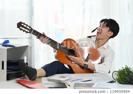Cheerful male employee with necktie around his head enjoying a music break amidst busy workday Cheerful male employee with necktie around his head enjoying a music break amidst busy workday 119930984