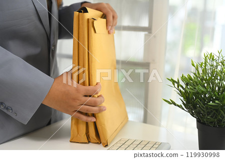 Cropped shot of businessperson organizing important documents in envelopes at office desk 119930998
