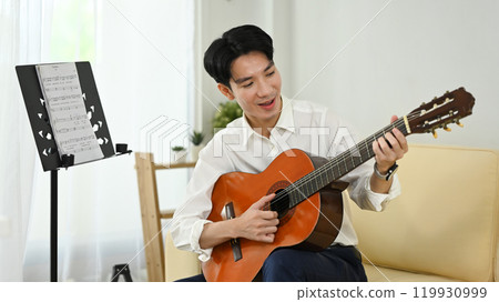 Happy asian man enjoying music practice in a bright living room 119930999