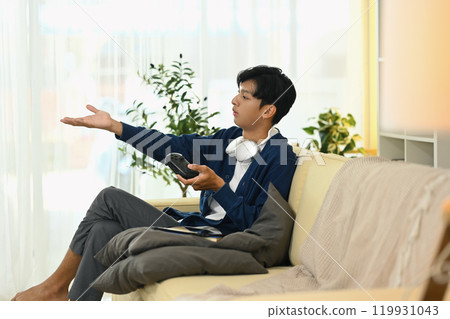 Smiling young asian man playing video game with joystick at home 119931043