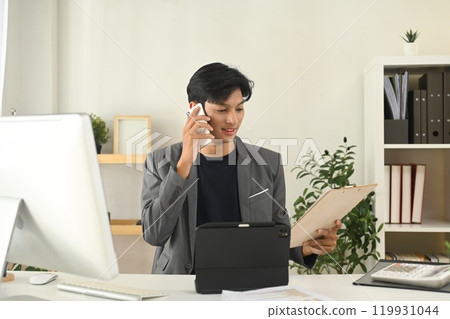 Young businessman having pleasant phone conversation at his office desk Young businessman having pleasant phone conversation at his office desk 119931044