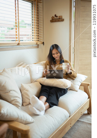 Smiling young woman using digital tablet in living room 119931075