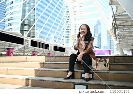 Confident mature businesswoman enjoying a phone conversation in modern city 119931101