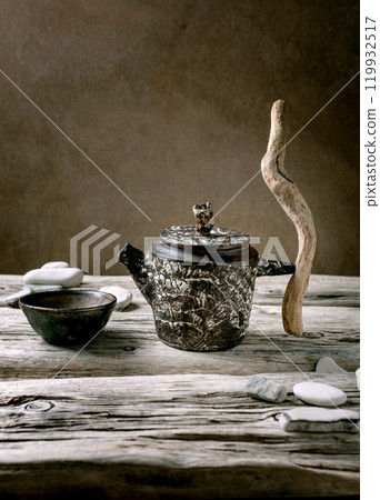 Original handmade ceramic teapot with wooden handle and cups for traditional Chinese tea drinking on an old wooden table. Decorative sea pebbles all around. Copy space 119932517