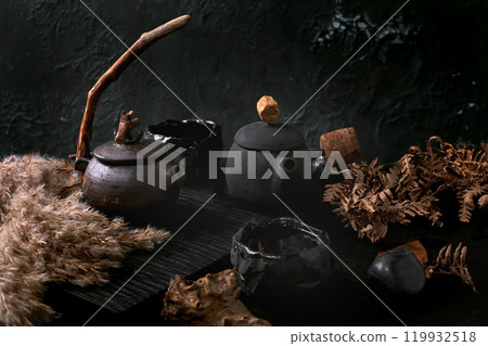 Chinese Tea Ceremony. Two traditional handmade ceramic black teapot with wooden handle on dark tea table. Autumn Vibe. Ceramic teacups and dried reed flowers side by side. 119932518