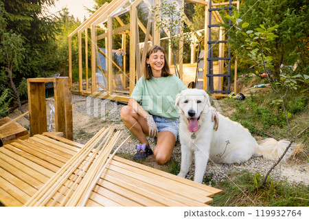 Female carpenter with her dog building wooden greenhouse 119932764