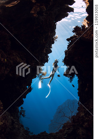 Woman freediver diving in underwater cave with rocks on Menjangan island, Bali. 119933008