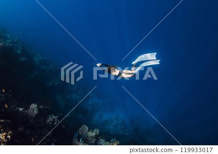 Female freediver swimming in underwater near reef rocks with blue water. Extreme activities 119933017