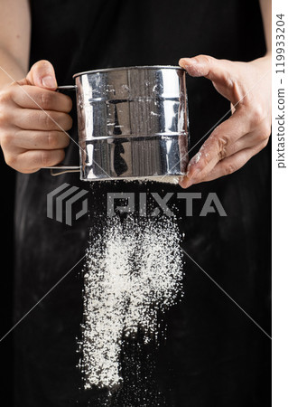 The cook sifts the wheat flour through a metal sieve. 119933204