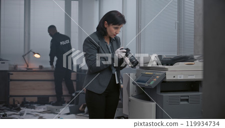 Female criminalist takes photos of evidence with camera. Policeman searches fingerprints Female criminalist takes photos of evidence with camera. Policeman searches fingerprints 119934734
