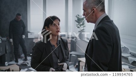 Female criminalist takes photos of evidence, then talks to male detective at crime scene Female criminalist takes photos of evidence, then talks to male detective at crime scene 119934765