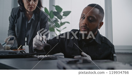 Close up of policeman searching for fingerprints on murder weapon, talking to female forensic scientist Close up of policeman searching for fingerprints on murder weapon, talking to female forensic scientist 119934766