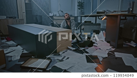 Dolly shot of depressed office worker sitting on the floor in destroyed office room Dolly shot of depressed office worker sitting on the floor in destroyed office room 119934849
