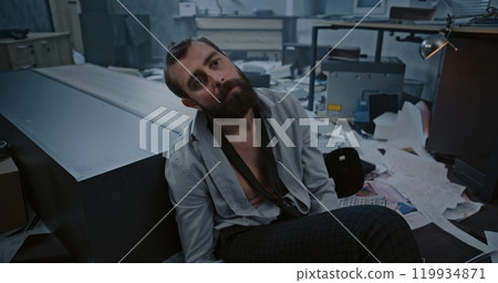 Stressed office employee in destroyed office room after firing Stressed office employee in destroyed office room after firing 119934871