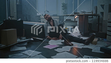 Frustrated office worker sits on the floor in destroyed office room Frustrated office worker sits on the floor in destroyed office room 119934886