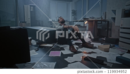 Dolly shot of frustrated office worker sitting on the floor in destroyed office room 119934952