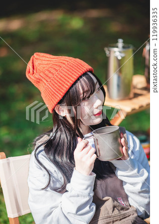 Young woman wearing knitted hat relaxing with a drink in camp Young woman wearing knitted hat relaxing with a drink in camp 119936335