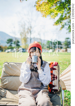 戴著針織帽的年輕女子在營地喝酒放鬆 119936342