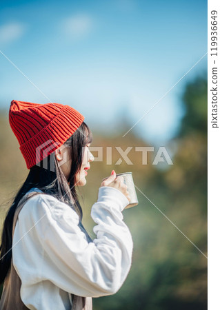 戴針織帽的年輕女子在藍天下喝飲料 戴針織帽的年輕女子在藍天下喝飲料 119936649