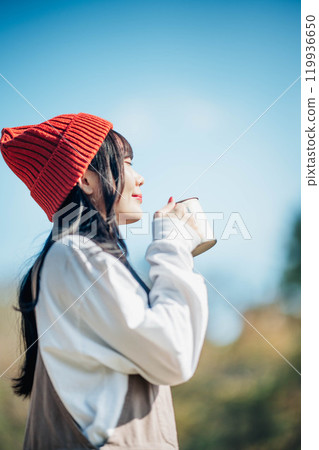戴針織帽的年輕女子在藍天下喝飲料 戴針織帽的年輕女子在藍天下喝飲料 119936650