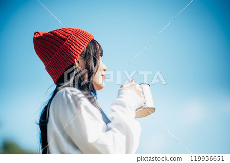 戴針織帽的年輕女子在藍天下喝飲料 119936651