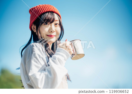 戴針織帽的年輕女子在藍天下喝飲料 戴針織帽的年輕女子在藍天下喝飲料 119936652