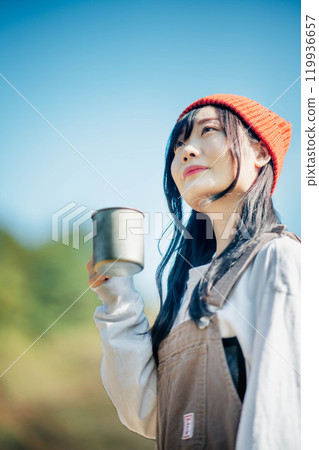 A young woman wearing a knitted hat drinking a drink under a blue sky 119936657