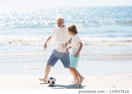 Grandfather and kids play football on beach. 119937618