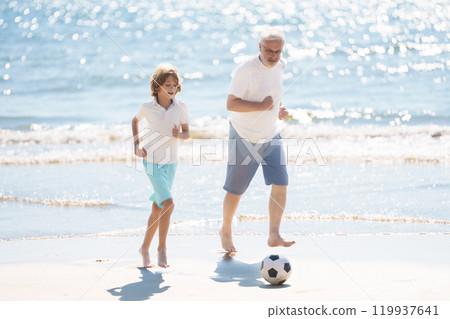 Grandfather and kids play football on beach. 119937641