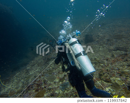 A scuba diver is blowing air bubbles and swimming past beautiful corals underwater A scuba diver is blowing air bubbles and swimming past beautiful corals underwater 119937842
