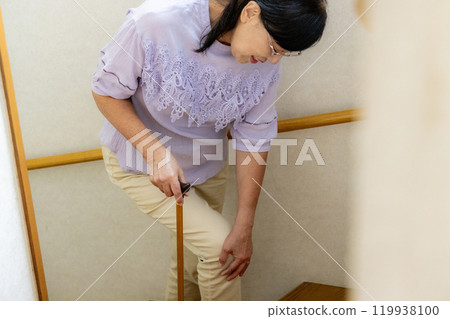 Senior woman with knee pain on stairs 119938100