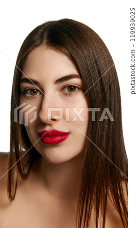 Close up of young attractive woman with brunette hair and bold red lips looking at camera with serene expression against white background. 119939025