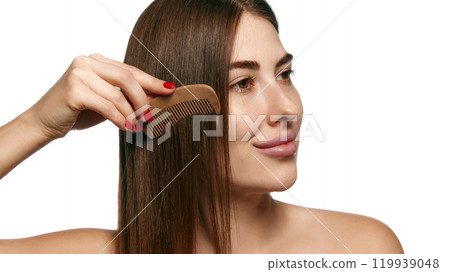 Woman combing her long hair with wooden comb, highlighting natural hair care against white background. Woman combing her long hair with wooden comb, highlighting natural hair care against white background. 119939048