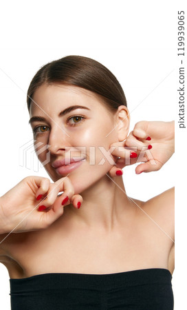 Close-up of young brunette woman massaging her jawline with both hands, emphasizing facial care against white background. 119939065