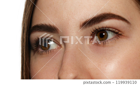 Close-up photo of young woman with bright brown eyes, long lashes and smooth facial skin against white background. 119939110