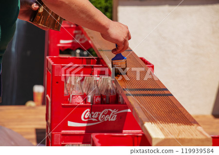 Close up of male hands holding a brush and painting a rough varnish on the background of the surface of a wooden board Close up of male hands holding a brush and painting a rough varnish on the background of the surface of a wooden board 119939584