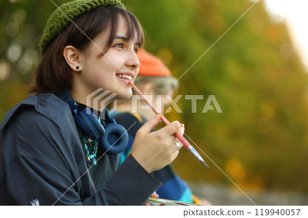 Creative Spirit. The Young Artist in Nature. a young female artist passionately painting outdoors, with brushes and paints in her hands. Surrounded by the beauty of nature, she is fully immersed in 119940057