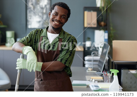 Waist up portrait of young African American man working in cleaning service and wearing uniform standing in office interior and smiling at camera, copy space Waist up portrait of young African American man working in cleaning service and wearing uniform standing in office interior and smiling at camera, copy space 119941173