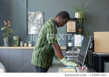 Side view portrait of young African American man cleaning desk at office workplace and wearing rubber gloves, copy space Side view portrait of young African American man cleaning desk at office workplace and wearing rubber gloves, copy space 119941183