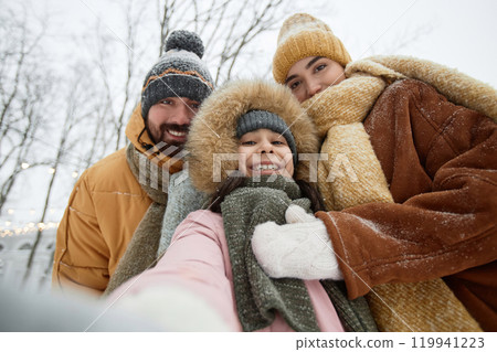 POV shot of modern young family with daughter taking selfie photo outdoors in winter park or speaking by video chat and smiling at camera 119941223