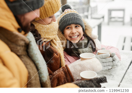 Portrait of happy young girl looking up at mother and father while enjoying hot cocoa at outdoor cafe in winter 119941230