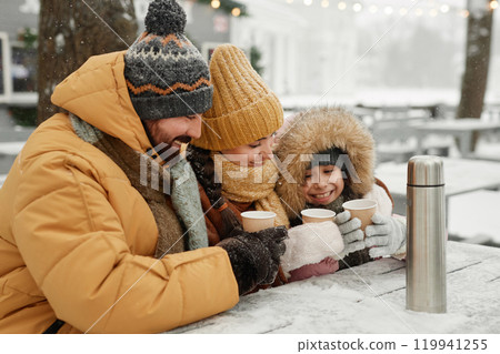 Portrait of modern young family drinking hot cocoa outdoors in winter sitting at cafe table together and smiling happily 119941255