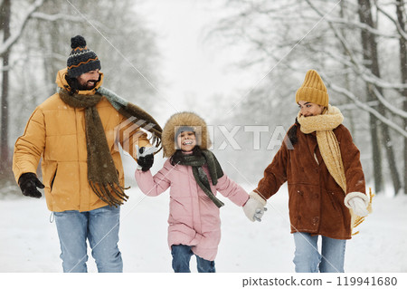 Happy family holding hands with smiling daughter and running towards camera in white winter park enjoying weekend together 119941680