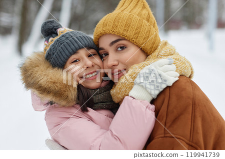Portrait of happy young mother and daughter embracing playfully and looking at camera having fun in winter outdoors 119941739