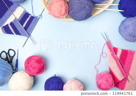 Blue, pink and beige knitting balls in basket with knitting needles and knitted scarf on blue background. Set for the hobby of knitting warm clothes or toys. Concept needlework 119941761