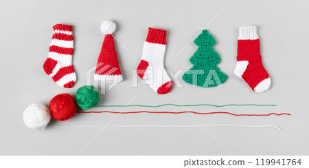 Knitted Christmas toys in form of red and white socks, Santa Claus hats, green Christmas trees with knitting balls on gray background. Top view, flat lay. Knitted Christmas toys in form of red and white socks, Santa Claus hats, green Christmas trees with knitting balls on gray background. Top view, flat lay. 119941764