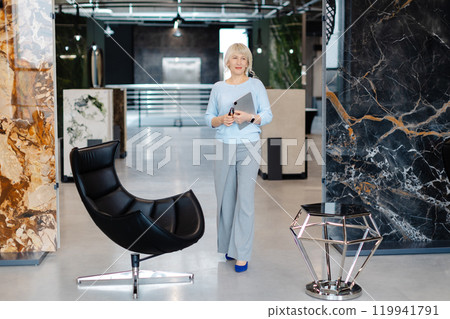 Confident Businesswoman Holding Tablet in Modern Office Setting Confident Businesswoman Holding Tablet in Modern Office Setting 119941791