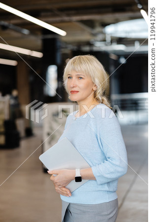Confident Businesswoman Holding Tablet in Modern Office Setting 119941796