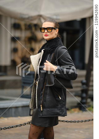 Stylish woman wearing a black coat and sunglasses during a fall day in an urban setting Stylish woman wearing a black coat and sunglasses during a fall day in an urban setting 119942690
